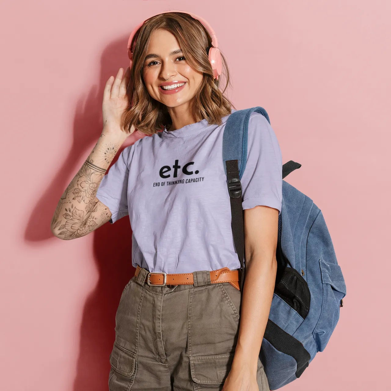 Woman wearing a 'etc.' t-shirt with a backpack on a pink background