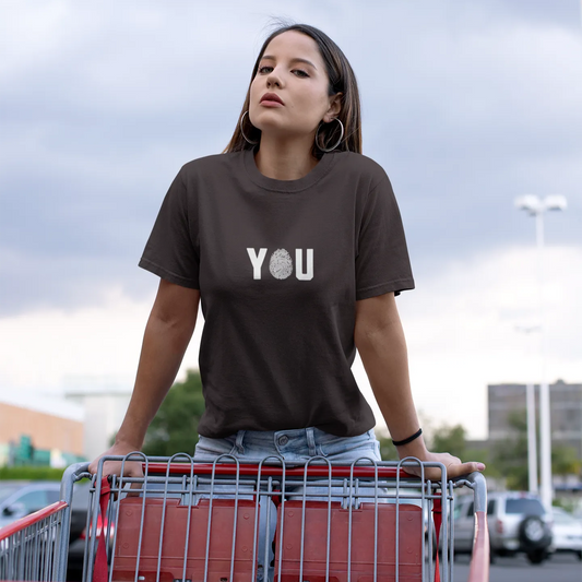 Woman wearing a brown t-shirt with 'YOU' printed on it, standing next to a shopping cart.