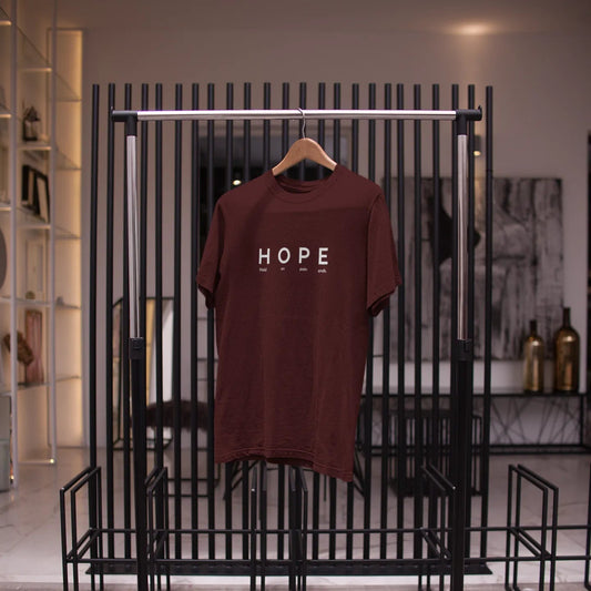 Brown t-shirt with 'HOPE' printed on it hanging on a black metal rack.