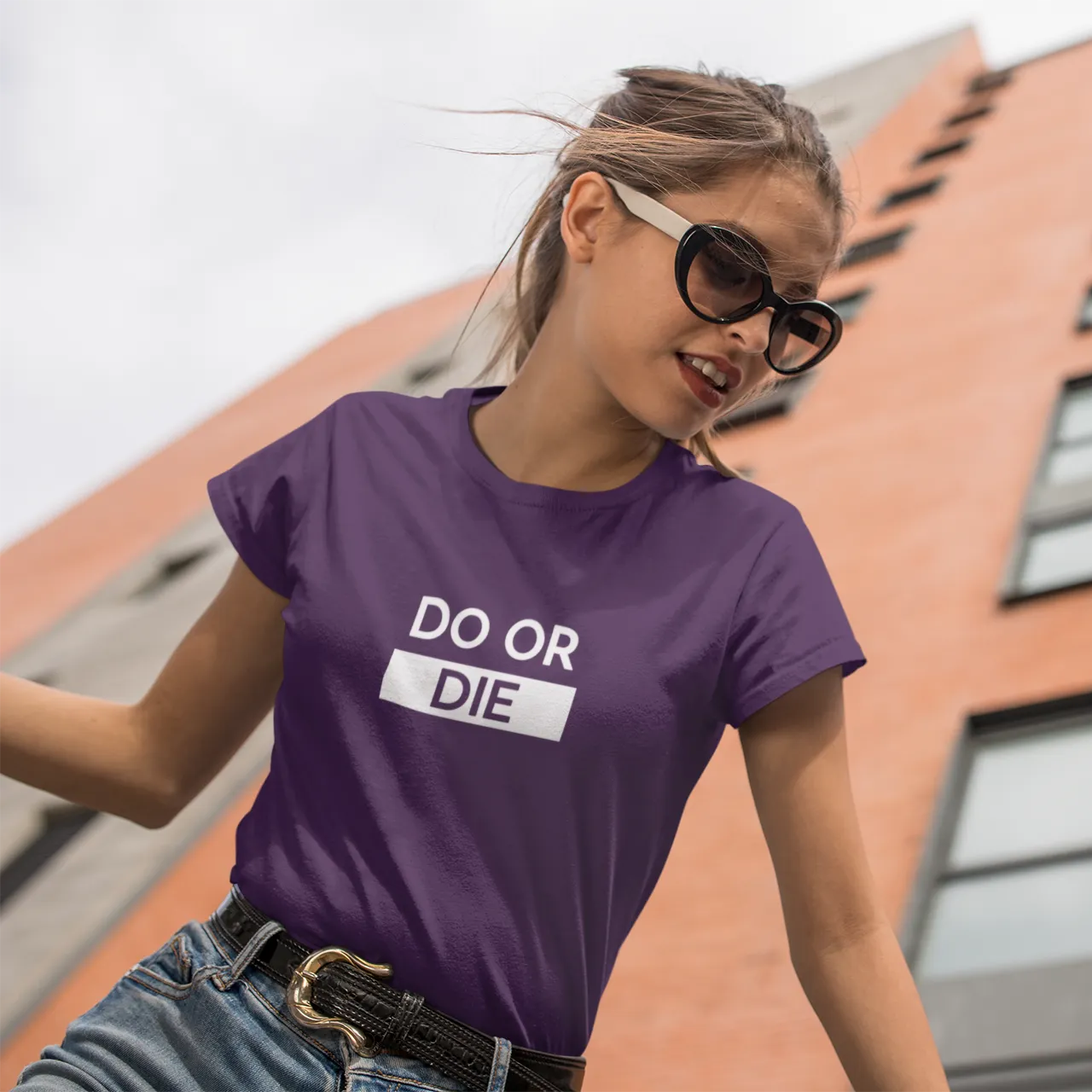 Woman wearing a purple t-shirt with 'DO OR DIE' text in front of a building.