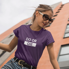 Woman wearing a purple t-shirt with 'DO OR DIE' text in front of a building.