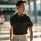 Man wearing a black polo shirt and light gray pants standing in an outdoor setting.