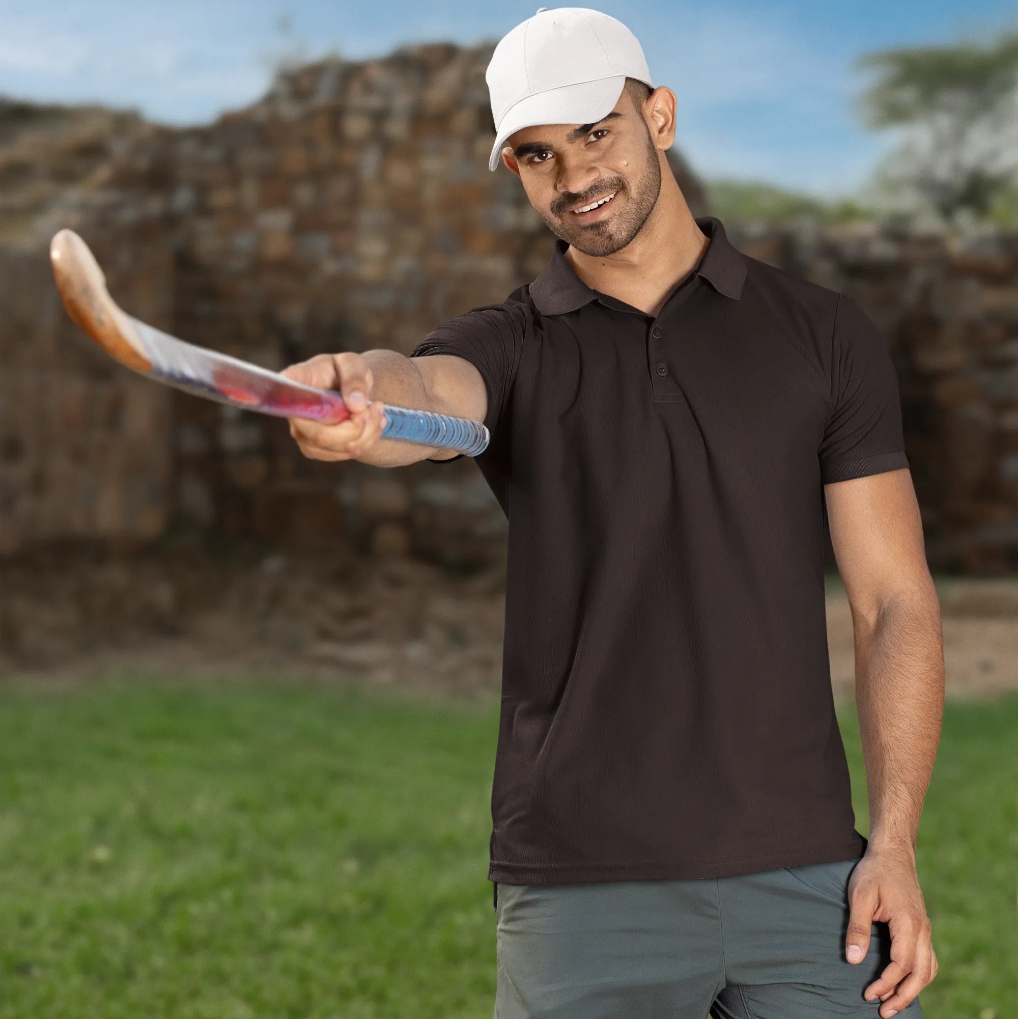 Man holding a hockey stick outdoors with a clear sky background