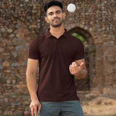 Man juggling a ball outdoors with a stone wall and grass in the background
