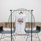 White t-shirt with text on a black metal chair against a white wall.