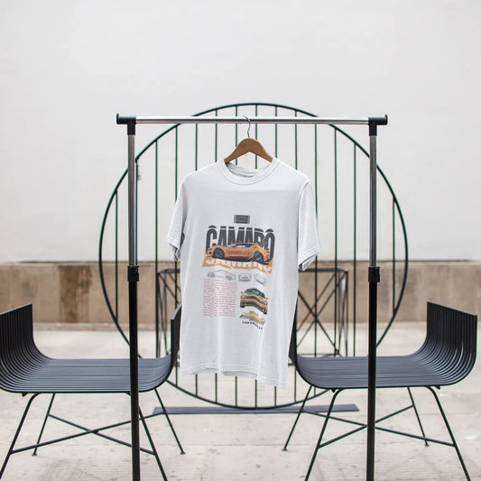 White t-shirt with graphic design on a black metal chair against a white wall.
