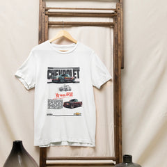White t-shirt with Chevrolet graphic on a wooden rack against a beige wall.