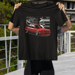 Person holding a black t-shirt with a red car graphic in an outdoor setting.