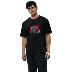 Man wearing a black t-shirt with a graphic design of a car and buildings, standing on a street.