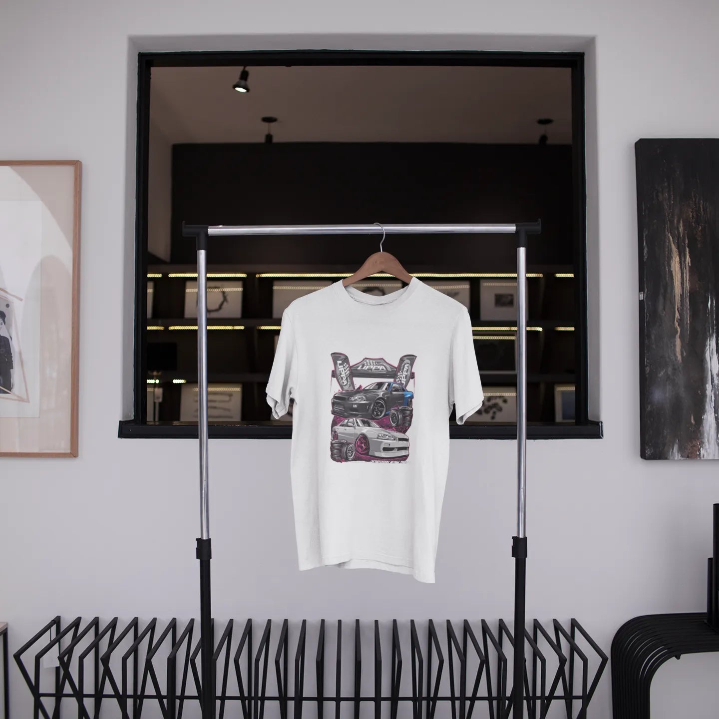White t-shirt with graphic design hanging on a rack in a modern interior setting.
