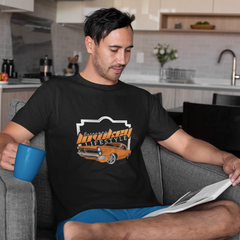Man sitting in a kitchen reading a newspaper, wearing a black t-shirt with a graphic design.