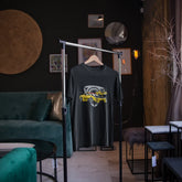 Black t-shirt with a graphic design on a hanger in a room with green sofa and wall decorations.