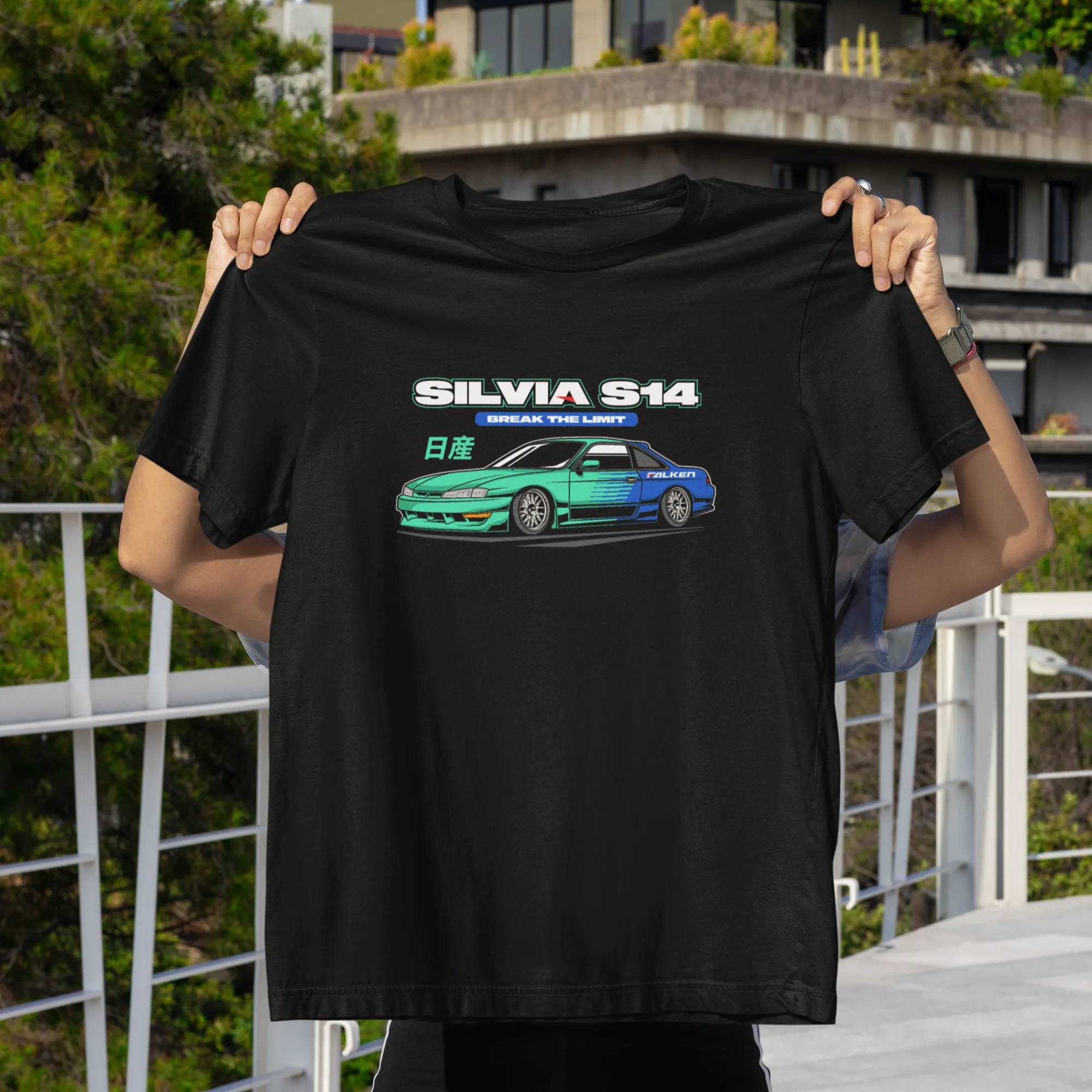 Person holding a black t-shirt with a car graphic and text in an outdoor setting.