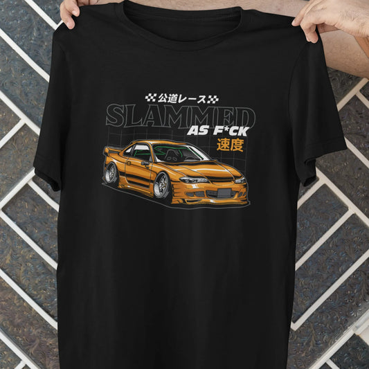 Black t-shirt with a car graphic and text held by a person against a tiled wall.