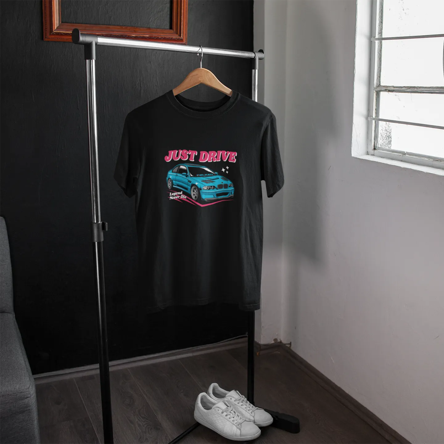 Black t-shirt with car graphic and 'Just Drive' text on a hanger in a room.
