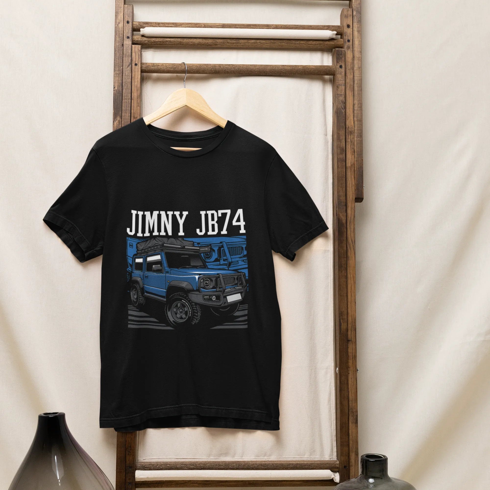 Black t-shirt with 'JIMNY JB74' design hanging on a wooden rack against a white wall.
