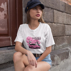 Woman wearing a white t-shirt with a car graphic sitting against a brick wall.