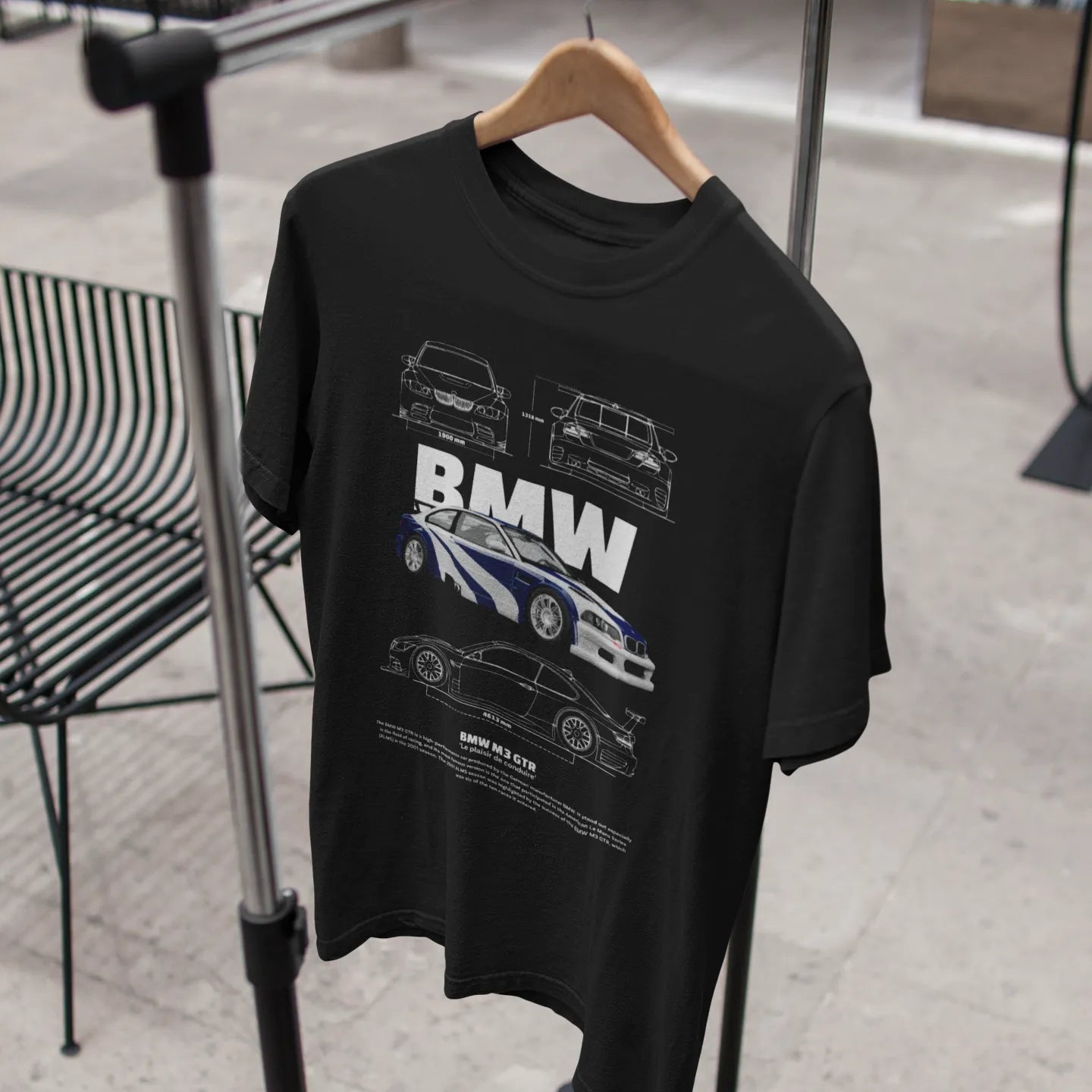 Black t-shirt with BMW car design on a hanger against a blurred indoor background