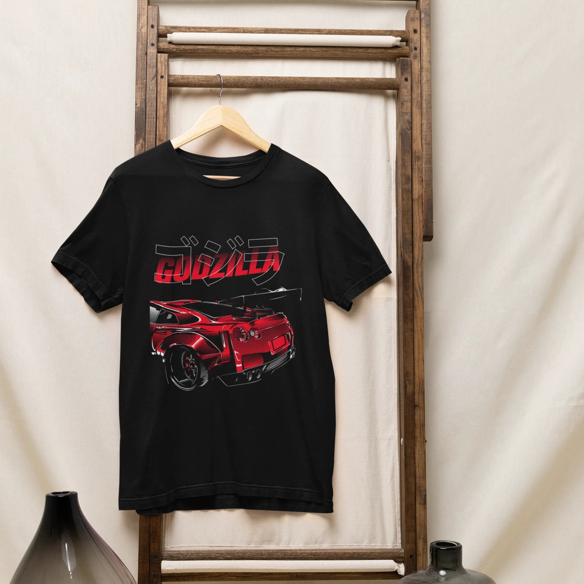 Black t-shirt with red and white graphic design on a wooden rack against a white wall.