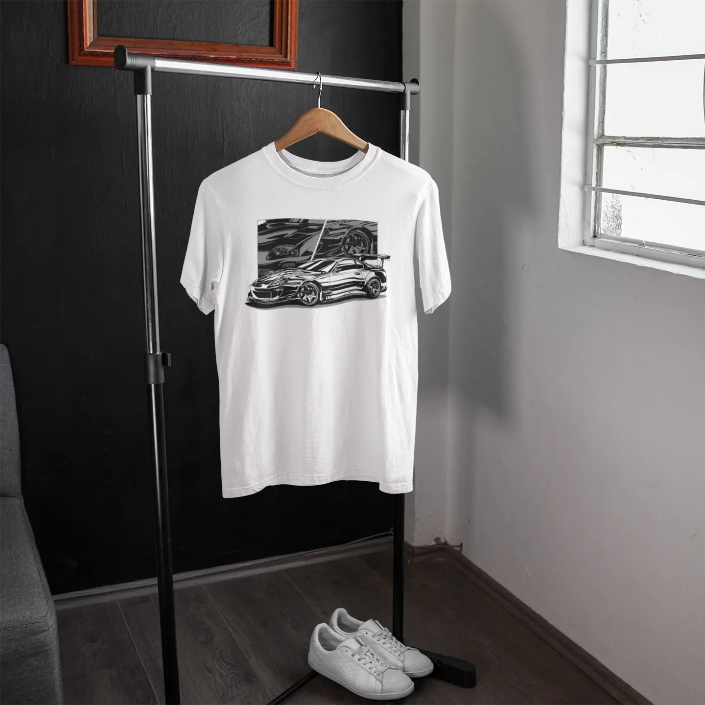 White t-shirt with a graphic design on a hanger in a room with a window.