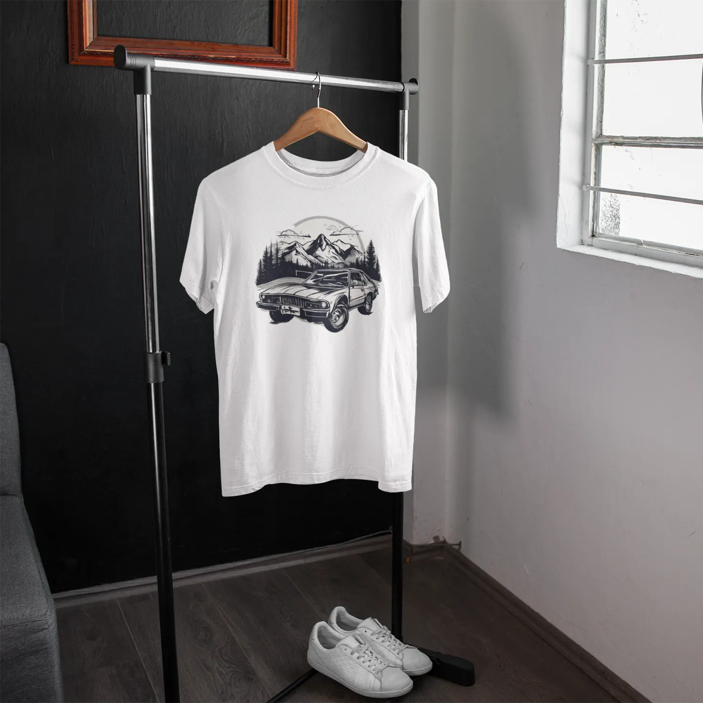 White t-shirt with graphic design hanging on a rack in a room with a window.