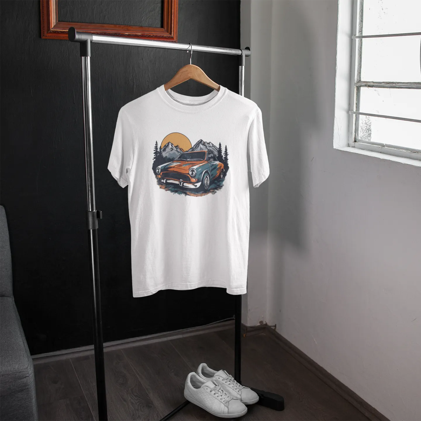 White t-shirt with a graphic design of a vintage car and mountains on a hanger in a room.