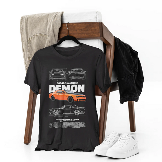 Black t-shirt with car graphics and text on a chair with white sneakers and gray pants.