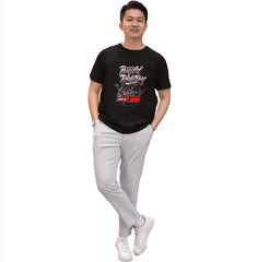 Person wearing a black t-shirt with graphic design and light gray pants on a white background