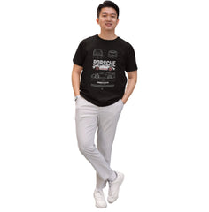Man wearing a black t-shirt with Porsche logo and white pants on a white background