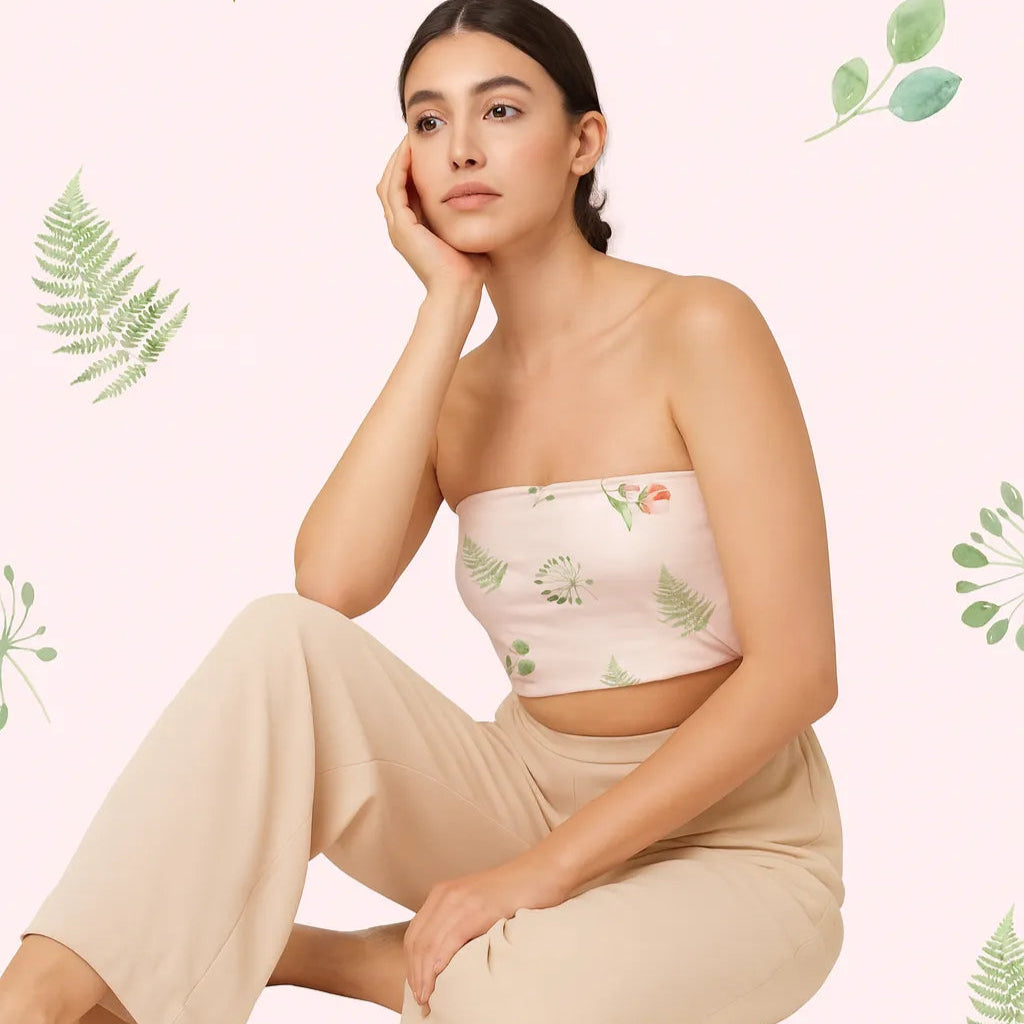 Woman wearing a floral strapless top and beige pants against a light pink background with green leaf patterns.