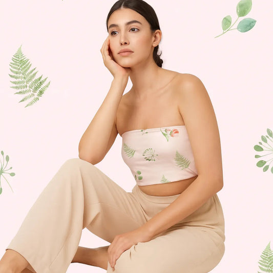 Woman wearing a floral strapless top and beige pants against a light pink background with green leaf patterns.