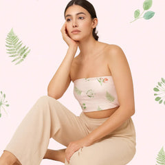 Woman wearing a floral strapless top and beige pants against a light pink background with green leaf patterns.