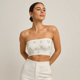 Woman wearing a white strapless top with floral embroidery on a plain background