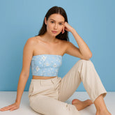 Woman wearing a light blue floral strapless top and beige pants against a blue background