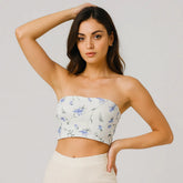 Woman wearing a strapless floral top and white pants against a plain background