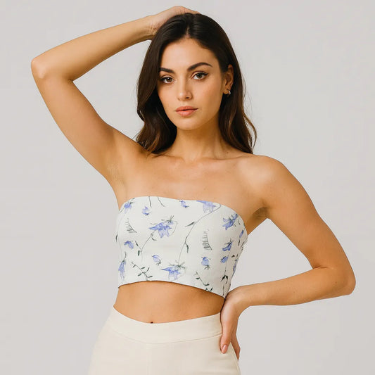 Woman wearing a strapless floral top and white pants against a plain background