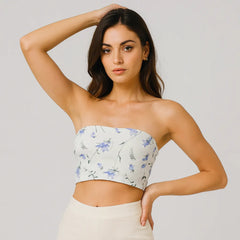 Woman wearing a strapless floral top and white pants against a plain background