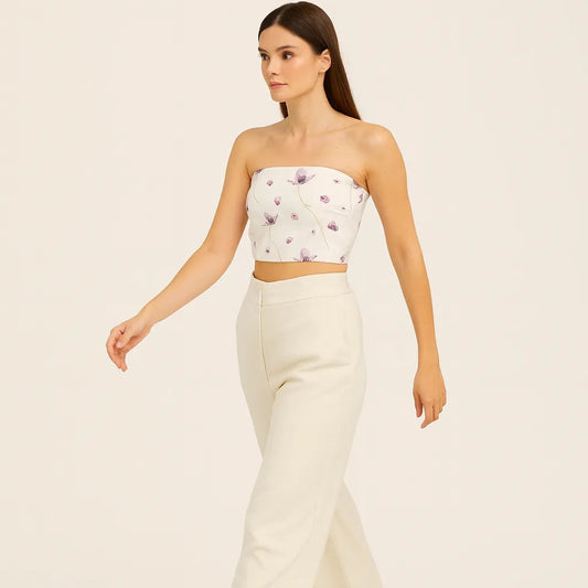 Woman wearing a strapless floral top and white pants on a beige background