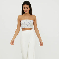 Woman wearing a strapless floral top and white wide-leg pants on a plain background