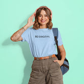Person wearing a light blue t-shirt with 'BE ORIGINAL' text, brown pants, and pink headphones on a teal background.