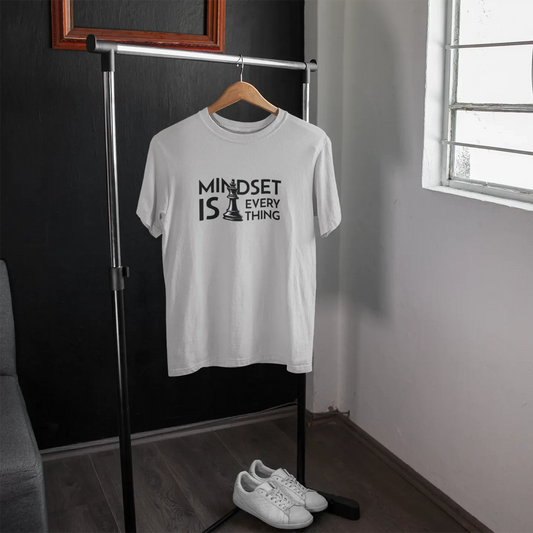 White t-shirt with 'MINDSET IS EVERYTHING' text on a hanger in a room with a window.