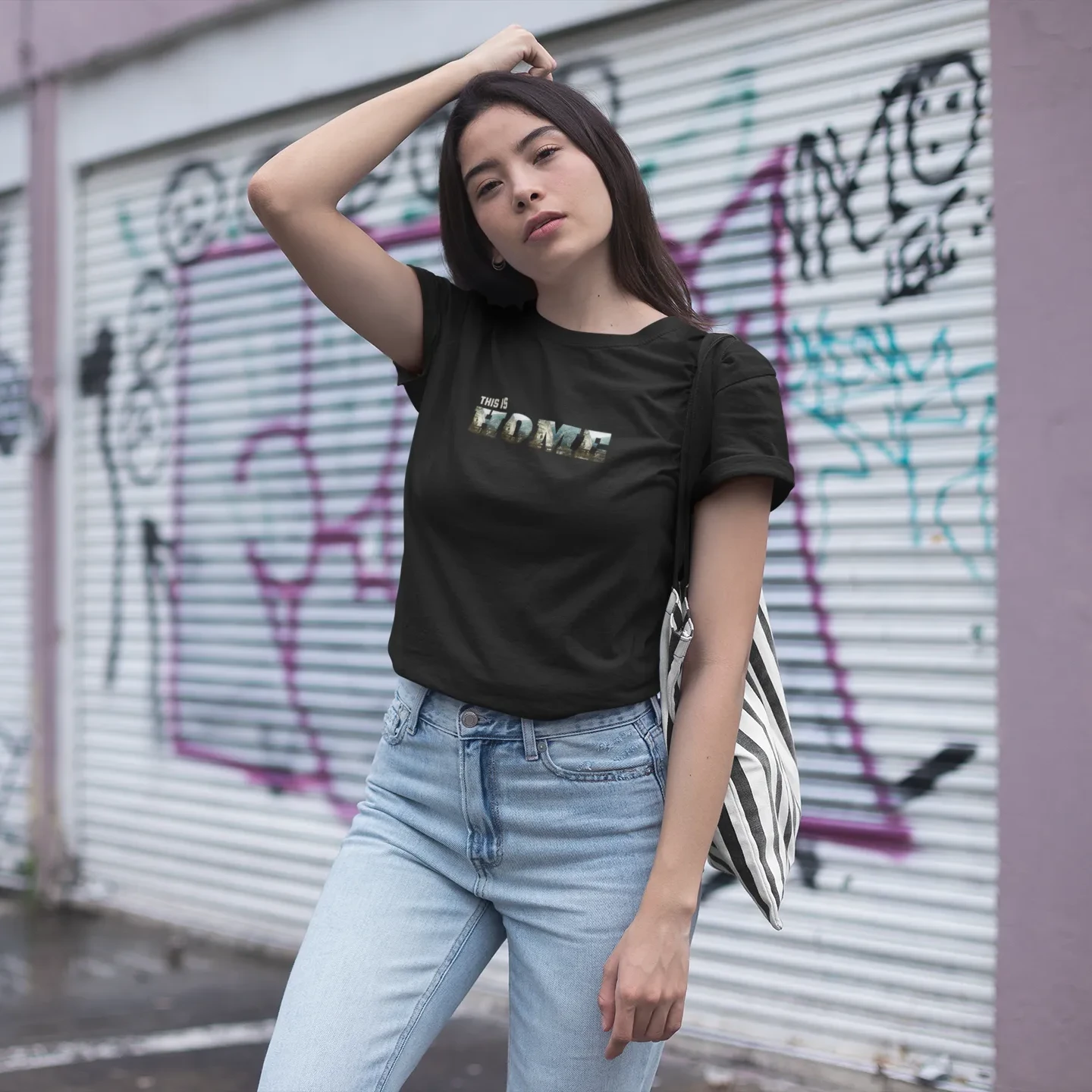 Woman wearing a black t-shirt with text and light blue jeans standing in front of a graffiti-covered wall.