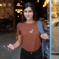 Woman wearing a brown t-shirt with a llama design, holding a phone, standing in a casual setting.
