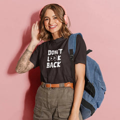 Woman wearing a black t-shirt with 'DON'T LOOK BACK' text, holding a blue backpack against a pink background