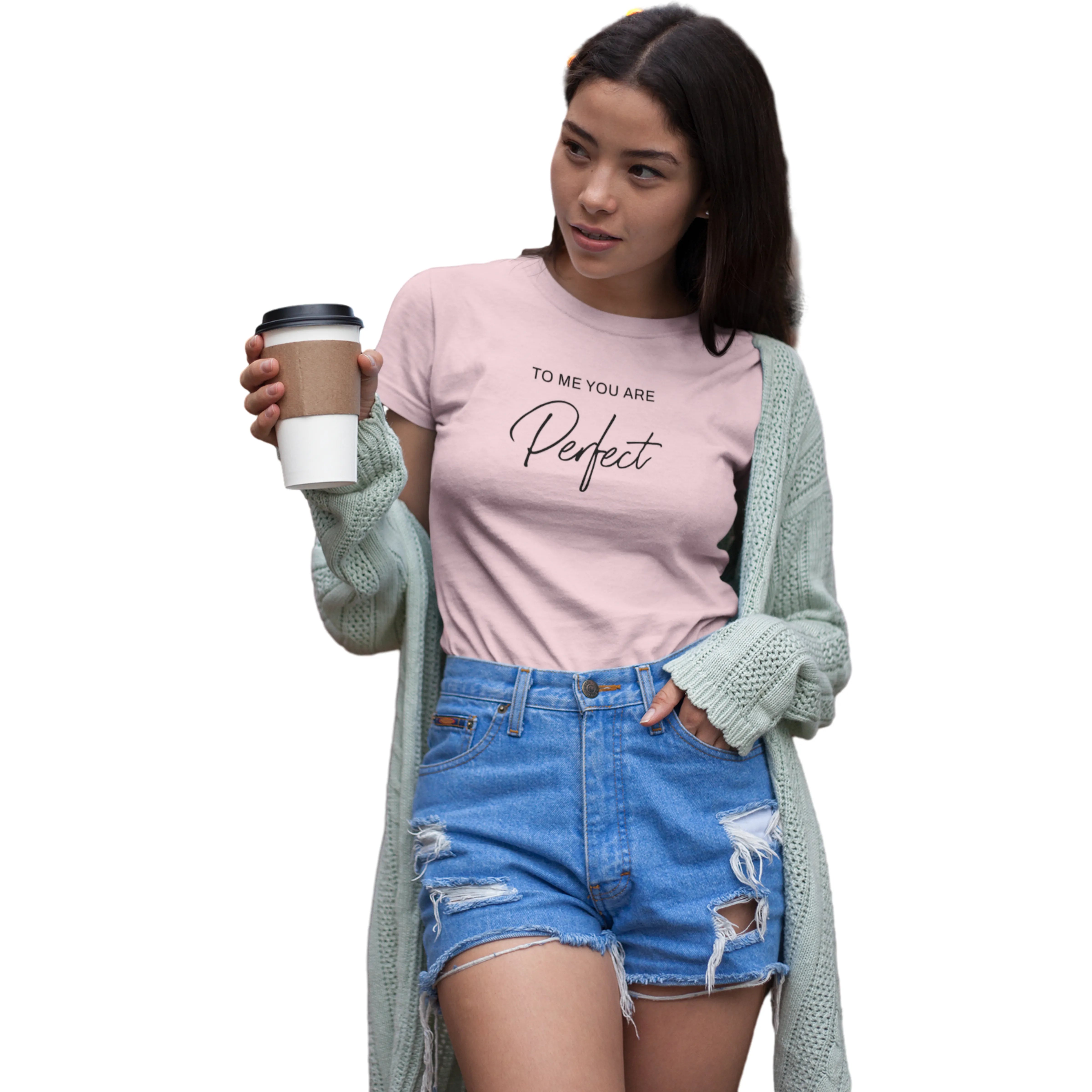 Woman wearing a pink t-shirt with text, holding a coffee cup, and wearing a light green cardigan and blue shorts on a white background.