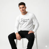 Man wearing a white long-sleeve shirt with text sitting on a white chair against a light gray background