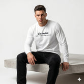 Man wearing a white long-sleeve shirt with text sitting on a concrete bench.