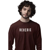 Man wearing a brown sweatshirt with 'REVERIE' printed on it against a white background