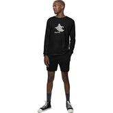 Man wearing a black long-sleeve shirt with a ghost graphic and shorts on a white background