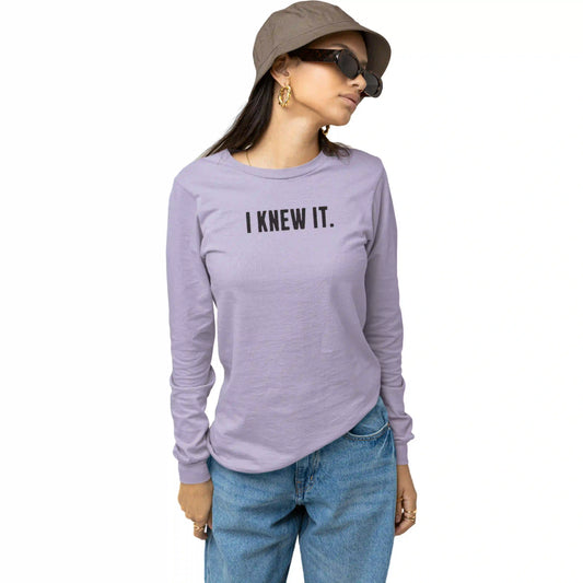Person wearing a purple long-sleeve shirt with 'I KNEW IT.' text, blue jeans, and a brown hat on a white background